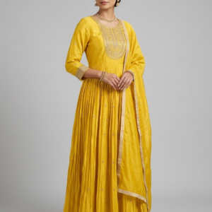 Front view of a model wearing a floor-length mustard yellow silk Anarkali suit featuring heavy gold zari and stonework embroidery on the neckline.